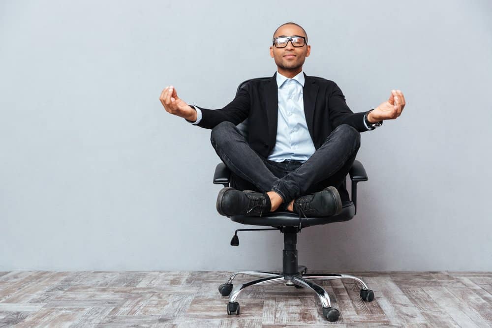 Man sitting with legs crossed in office chair with arms in yoga pose.