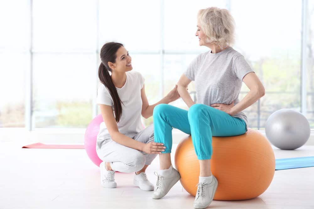 Older woman sitting on balance ball working with professional.