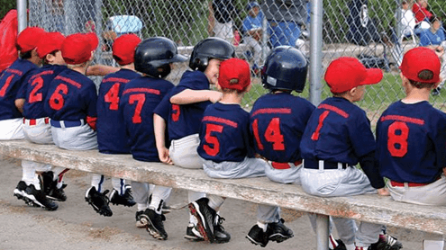 Little league baseball team sitting on bench during game.