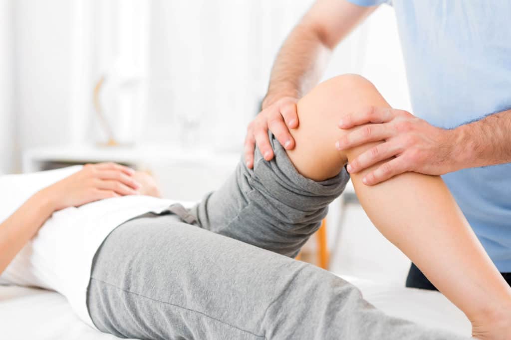 Physical therapist with hands on knee area of patient.